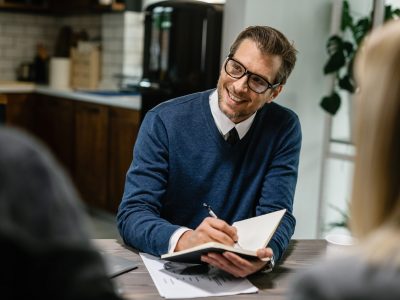 Happy financial advisor communicating with a couple and taking notes into his notebook.