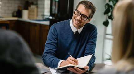 Happy financial advisor communicating with a couple and taking notes into his notebook.