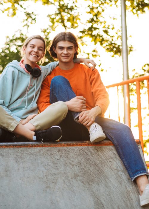 Young smiling boy and girl happily looking in camera spending time together in skatepark